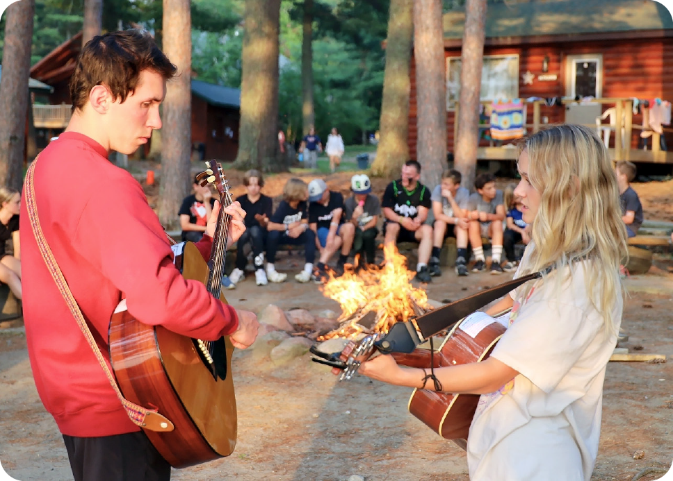 2 people playing guitar in front of a group of campers
